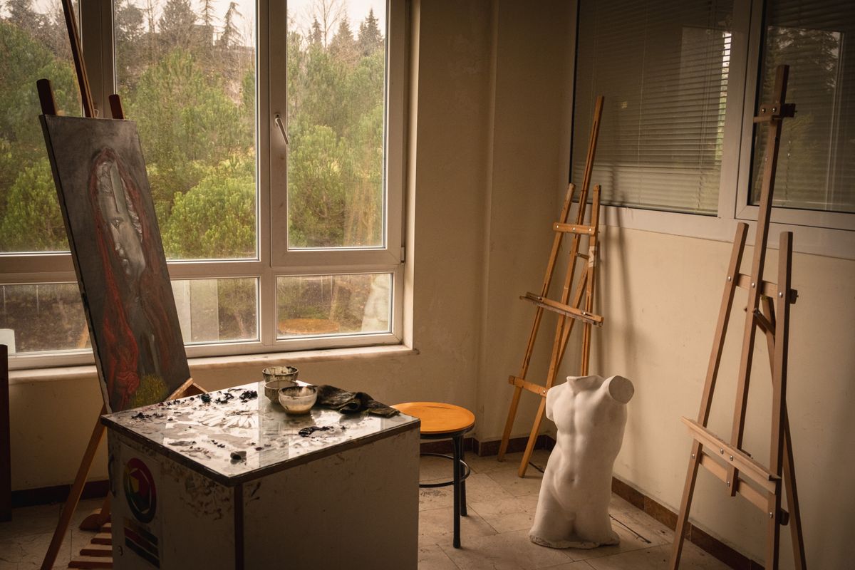 Un atelier d'artiste avec chevalet, tabourets et matériel, éclairé par une fenêtre